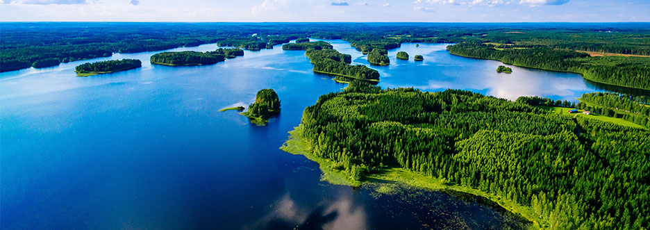 Luftaufnahme der finnischen Seenlandschaft mit grünen Inseln und dichtem Wald unter blauem Himmel – typisches Naturpanorama Finnlands im Sommer