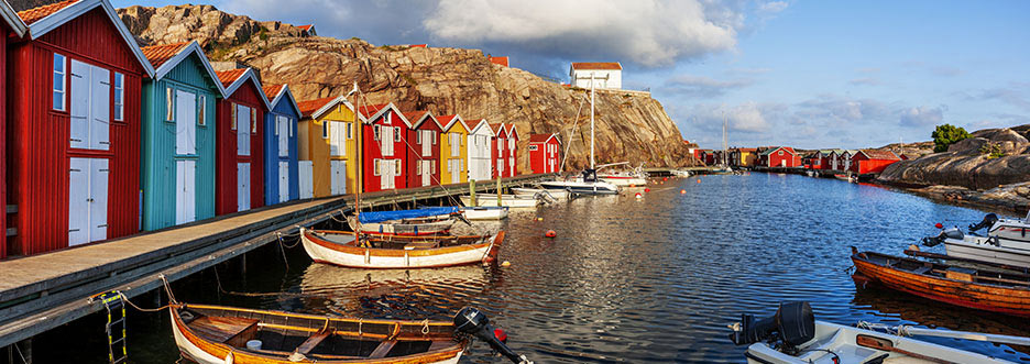 Bunte Bootshäuser am Wasser in einem schwedischen Fischerdorf mit kleinen Holzbooten im Vordergrund